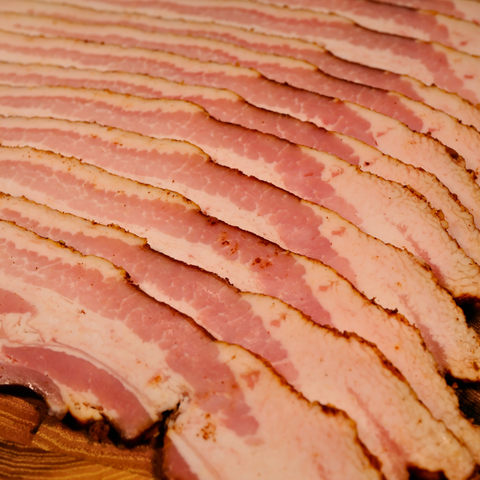 A close up of thick sliced smoked Apple Cinnamon Bacon on a wood surface.