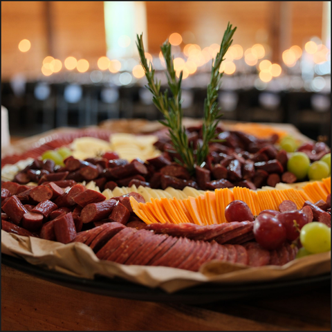 Platter of assorted meats, cheeses, and fruits with a decorative sprig on a blurred background.
