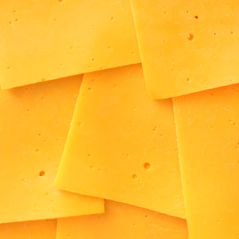 Close-up of several overlapping slices of bright yellow cheddar cheese with small holes, filling the frame.
