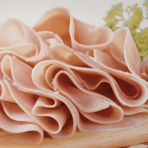 Thinly sliced chicken arranged in overlapping curls on a light wooden board with a small green herb garnish in the background.