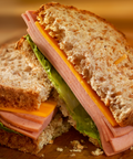 A close-up of a toasted whole wheat sandwich cut in half, filled with sliced bologna, cheese, and lettuce on a wooden surface.