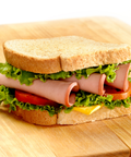 A classic bologna and cheese sandwich on a wooden cutting board, featuring white bread, sliced turkey, fresh green lettuce, tomato, and a slice of yellow cheese.