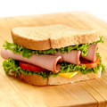 A classic bologna and cheese sandwich on a wooden cutting board, featuring white bread, sliced turkey, fresh green lettuce, tomato, and a slice of yellow cheese.