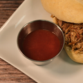 Pulled pork sandwich with a side of Chicago Sweet BBQ Sauce on a white plate.
