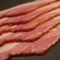 Close-up of sliced Premium Sugar Cured Double Smoked Bacon on a dark surface