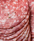 Close-up of sliced cured genoa salami, stacked with visible fat marbling and small herb flecks.