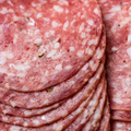 Close-up of sliced cured genoa salami, stacked with visible fat marbling and small herb flecks.
