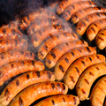 Grilled Italian Pork Brats with grill marks cooking on a hot grill with visible smoke rising.