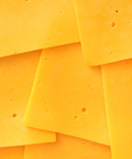 Close-up of several overlapping slices of bright yellow cheddar cheese with small holes, filling the frame.