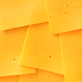 Close-up of several overlapping slices of bright yellow cheddar cheese with small holes, filling the frame.