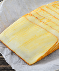 Sliced cheese sticks with golden-brown edges arranged on parchment paper over a dark wooden surface.