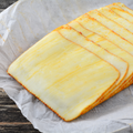 Sliced cheese sticks with golden-brown edges arranged on parchment paper over a dark wooden surface.