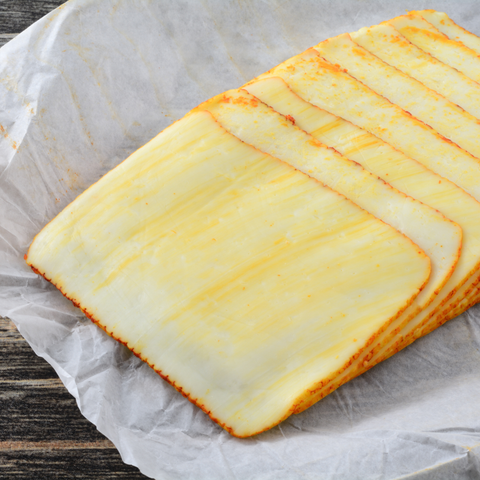 Sliced cheese sticks with golden-brown edges arranged on parchment paper over a dark wooden surface.