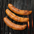 Three Nacho Cheese Brats cooking on a grill with grill marks.