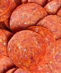 A close-up pile of round pepperoni slices showing the textured, seasoned meat surface with visible spices and small flecks.