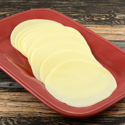 Thin round slices of pale yellow cheese arranged on a red rectangular serving platter, set on a dark wood surface.