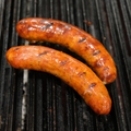 Two Sicilian Pizza Brats cooking on a grill with visible grill marks.