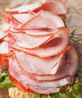 Slices of smoked ham layered over a sandwich with tomato and green lettuce on a piece of bread, set on a brown textured surface.