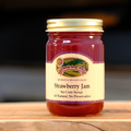 A jar of Country Smoke House Strawberry Jam on a wooden surface.