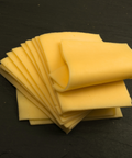 A stack of thick, pale yellow cheese slices fanned out on a dark, textured slate surface.