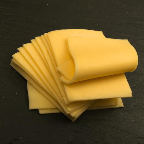 A stack of thick, pale yellow cheese slices fanned out on a dark, textured slate surface.