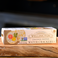 A box of Wellington Cracked Pepper Water Crackers placed on a wooden surface.