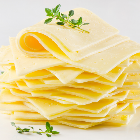 A stack of thin, pale yellow cheese slices with small holes, garnished with two small green herb sprigs, photographed on a clean white background.